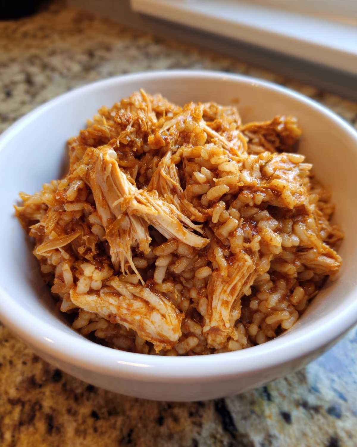 Close-up of shredded chicken mixed with seasoned brown rice in a white bowl, part of Instant Pot Chicken Burrito Bowls.