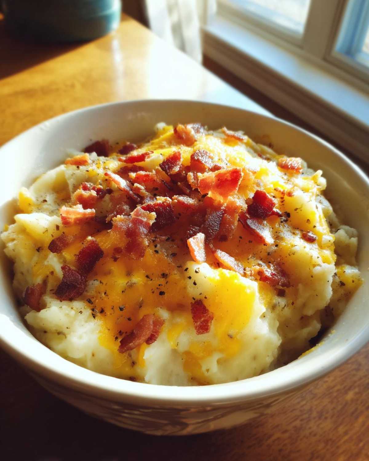 Close-up of a bowl of Instant Pot Creamy Potato Soup with Bacon, topped with melted cheddar cheese and crispy bacon bits.