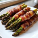 Close-up of perfectly cooked Keto Bacon Wrapped Asparagus Bundles stacked on a white plate.