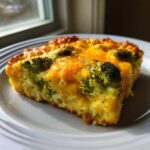 A close-up slice of Keto Cheesy Broccoli Casserole featuring bright green broccoli florets baked under a layer of melted, golden cheddar cheese.