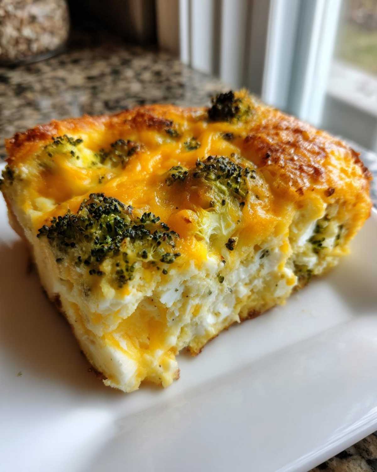 A close-up of a square serving of Keto Cheesy Broccoli Casserole with a golden-brown top and visible broccoli florets.