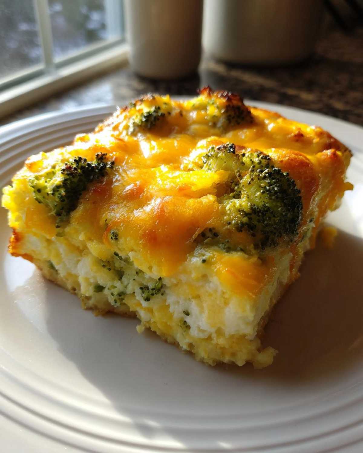 A square slice of Keto Cheesy Broccoli Casserole featuring a thick layer of melted cheddar cheese over broccoli and egg base.