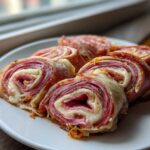 Close-up of five baked Keto Italian Sub Roll-Ups featuring layers of deli meat and melted white cheese.