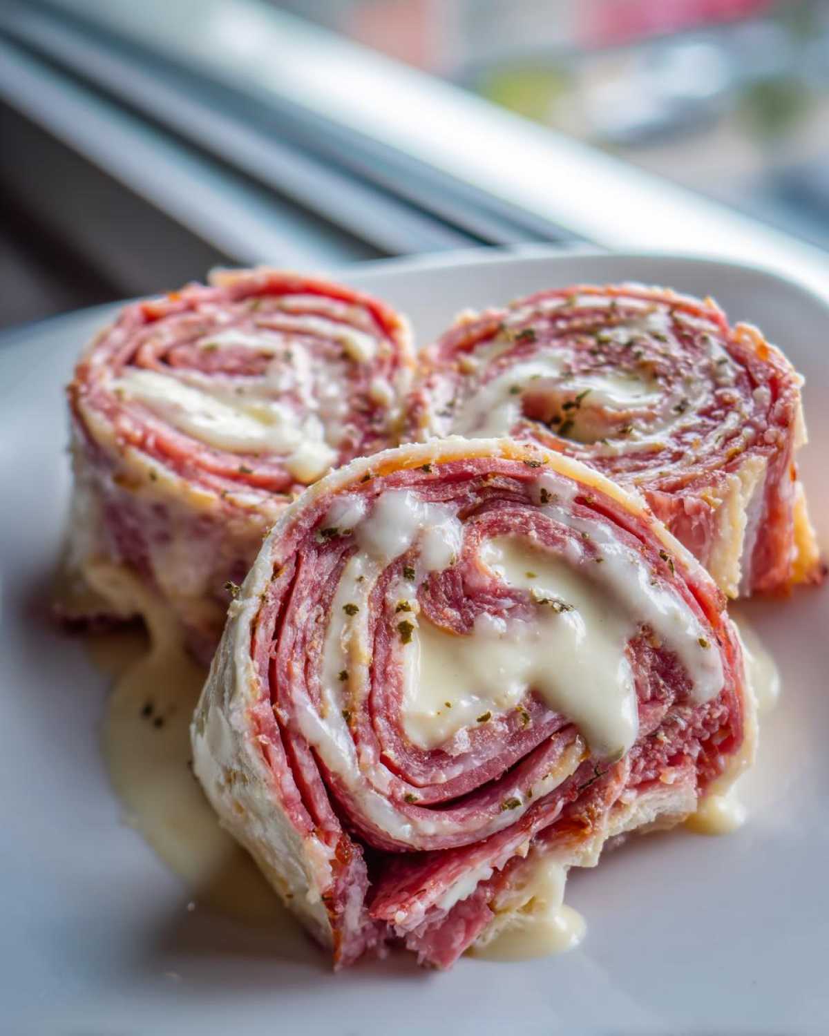 Three slices of Keto Italian Sub Roll-Ups showing layers of deli meat and melted white cheese, drizzled with sauce.