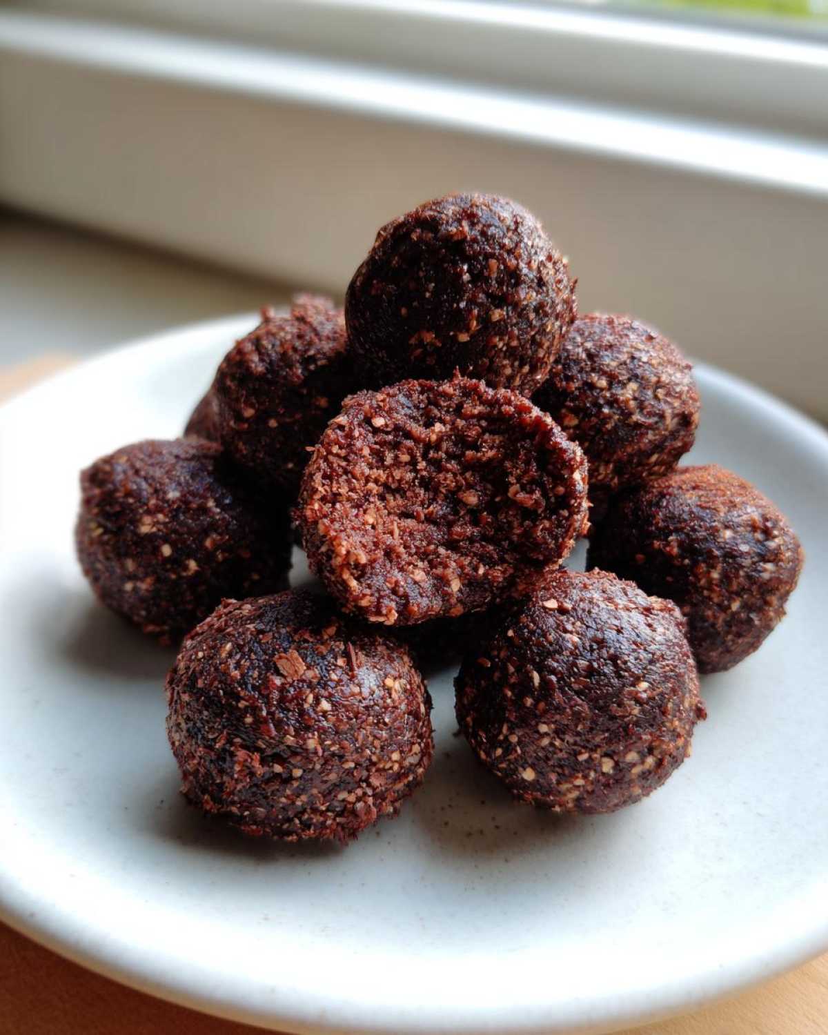 A small stack of rich, dark No-Bake Brownie Batter Protein Balls on a white plate.