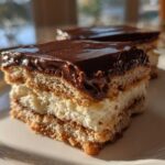 Close-up of a layered slice of No-Bake Chocolate Eclair Cake featuring graham crackers, creamy filling, and chocolate glaze.