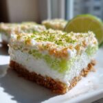 Close-up of a layered No-Bake Coconut Lime Bars slice with a graham cracker crust and lime zest topping.