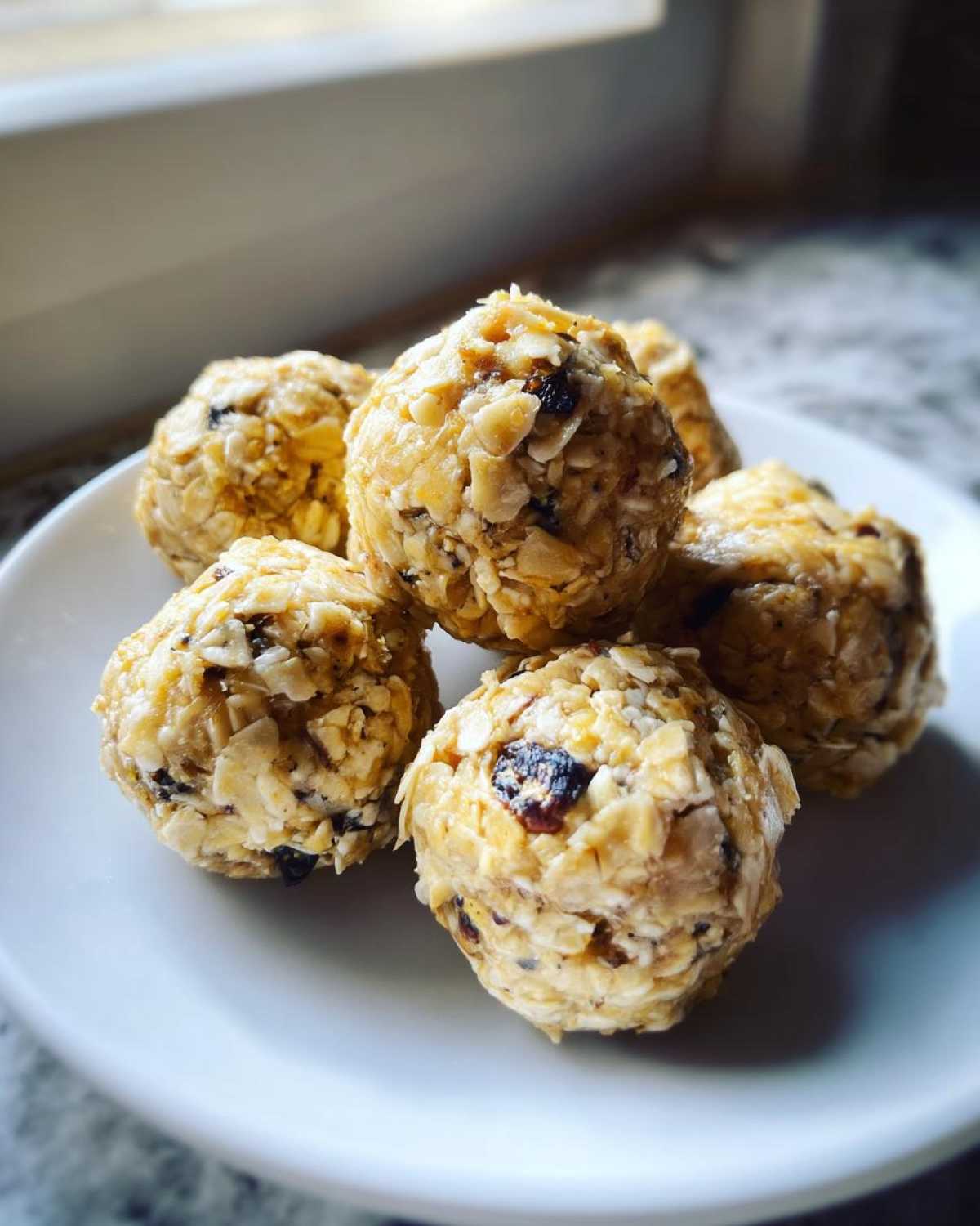 A small stack of No-Bake Lemon Blueberry Energy Bites made with oats and dried fruit on a white plate.
