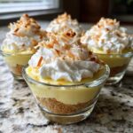 Four individual No-Bake Lemon Coconut Cream Pie Cups topped with whipped cream and toasted coconut.