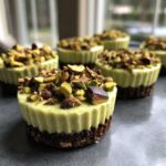 A close-up of several No-Bake Pistachio Cheesecake Cups with a dark crust and topped with chopped pistachios.