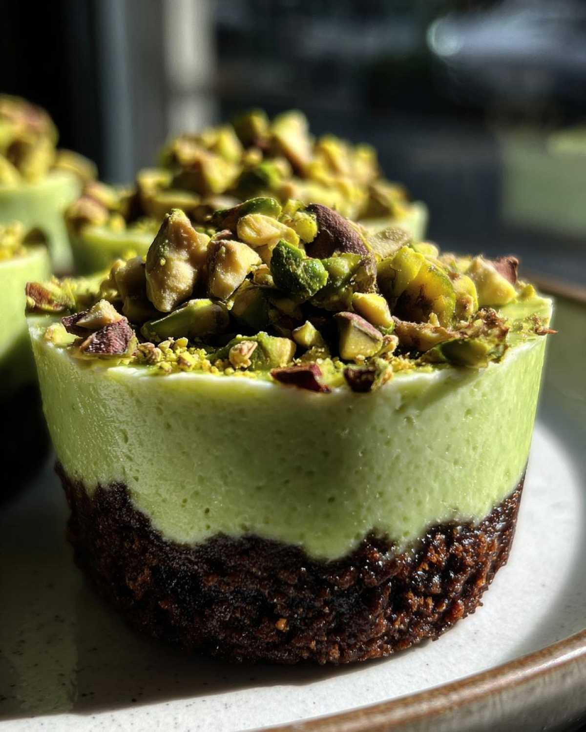 Close-up of a No-Bake Pistachio Cheesecake Cup with a dark crust and green filling topped with chopped pistachios.