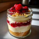 A layered No-Bake Raspberry White Chocolate Cheesecake Jar with graham cracker crust, creamy filling, and fresh raspberries on top.