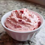 Close-up of fluffy pink No-Bake Strawberry Cheesecake Dip with visible strawberry pieces in a white bowl.