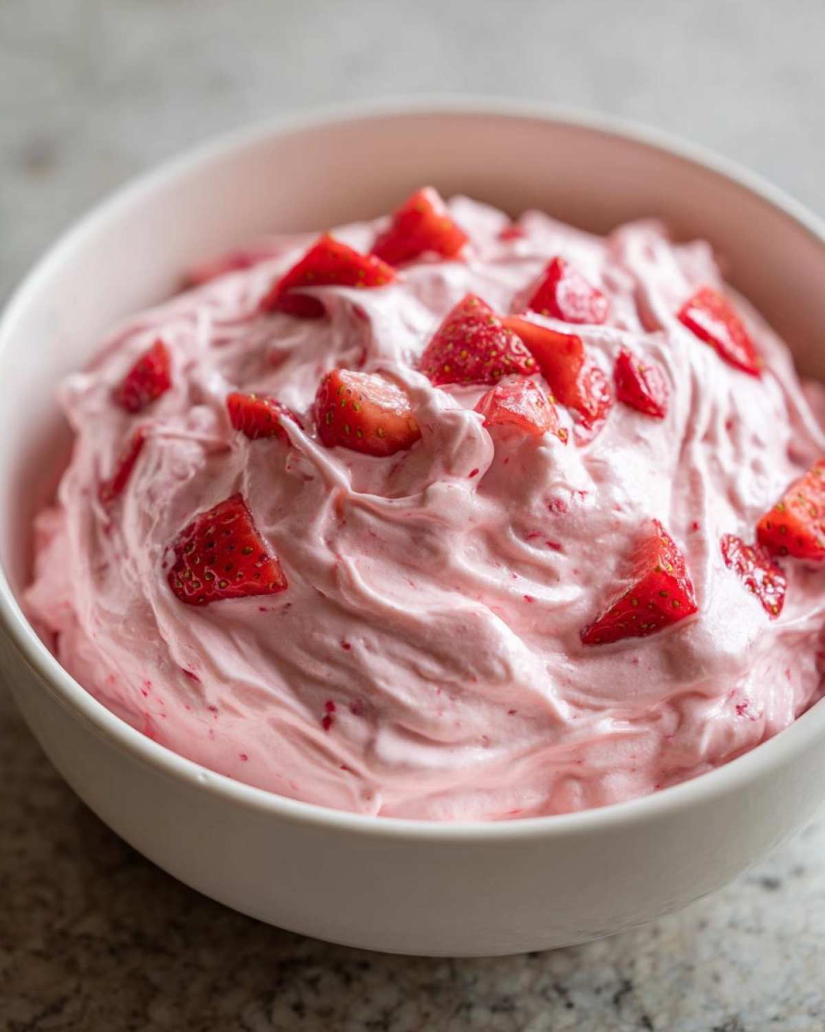 Close-up of fluffy pink No-Bake Strawberry Cheesecake Dip topped with fresh diced strawberries in a white bowl.