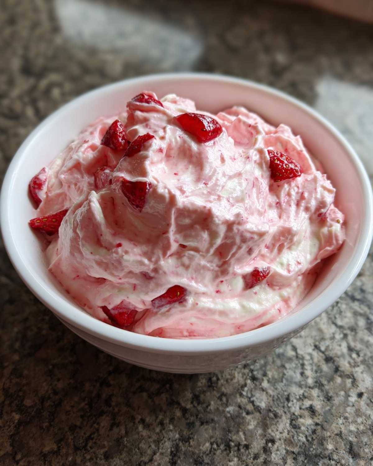 A close-up of fluffy pink No-Bake Strawberry Cheesecake Dip topped with diced strawberries in a white bowl.