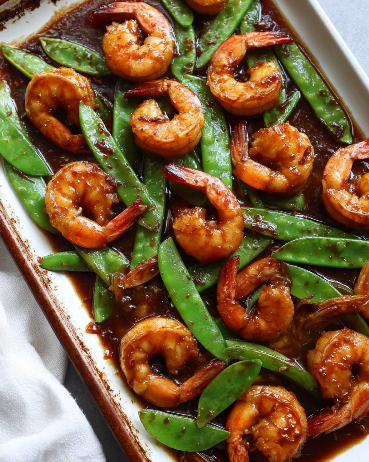Close-up of cooked shrimp and bright green snow peas coated in a rich honey garlic sauce.