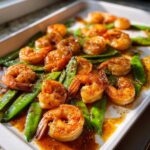 Close-up of glossy, glazed One-Pan Honey Garlic Shrimp and Snow Peas coated in sauce and pepper.