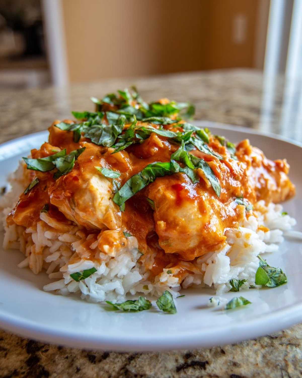 A close-up of One-Pot Creamy Tomato Basil Chicken and Rice served over white rice and topped with fresh basil.