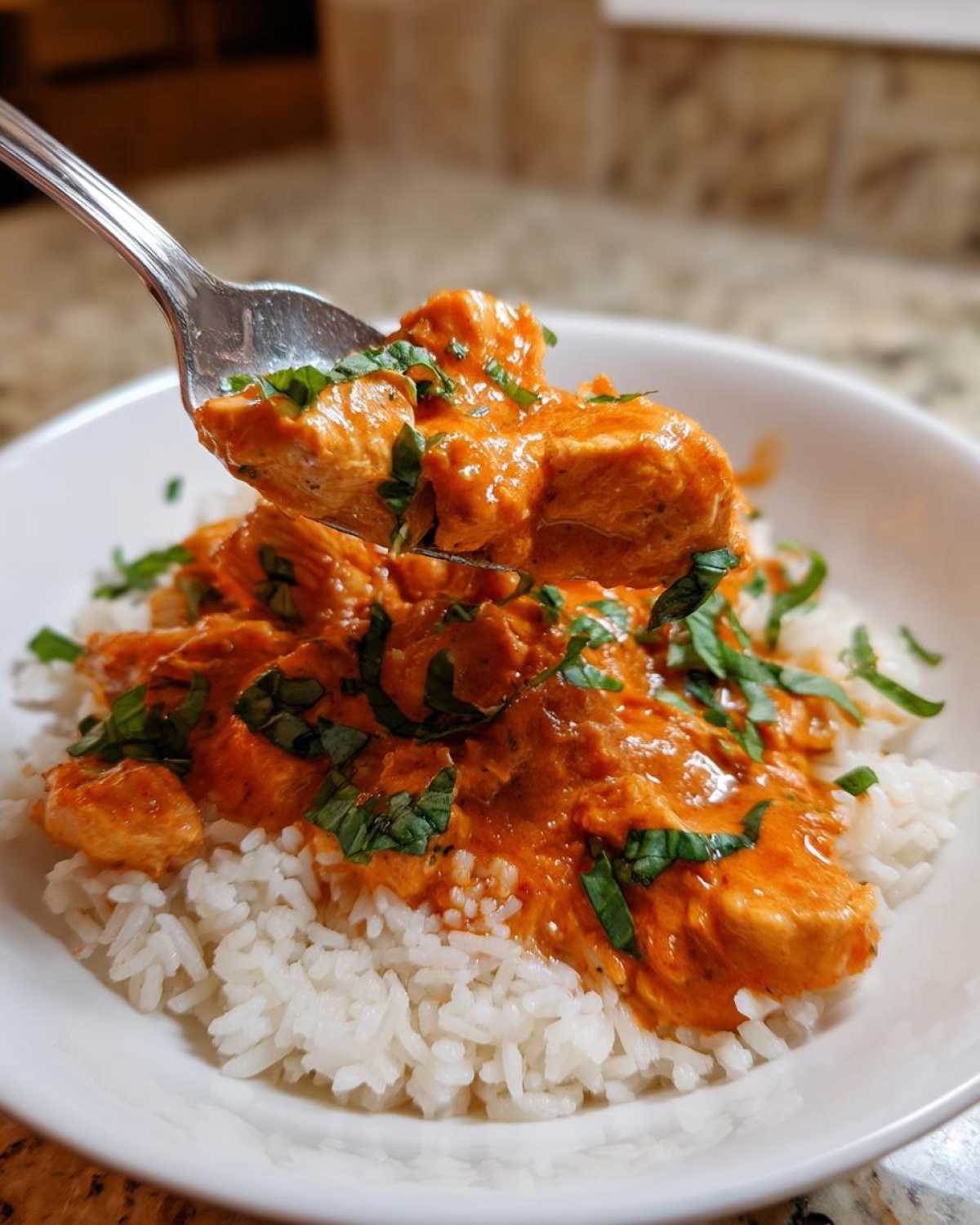 A fork lifting pieces of creamy tomato basil chicken and rice topped with fresh basil.