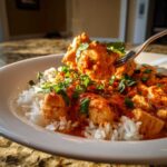 A fork lifts a piece of creamy tomato basil chicken and rice from a white bowl, garnished with fresh basil.