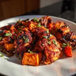 Close-up of Sheet Pan Harissa Chicken with Sweet Potatoes garnished with fresh parsley on a white plate.