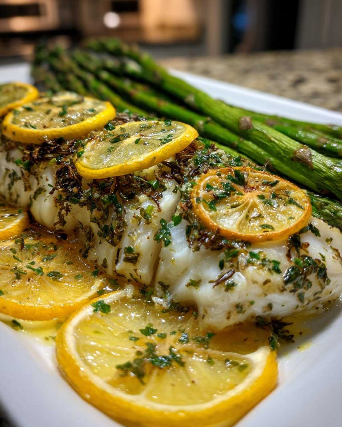 Close-up of flaky Sheet Pan Lemon Herb Cod with Asparagus topped with lemon slices and herbs.