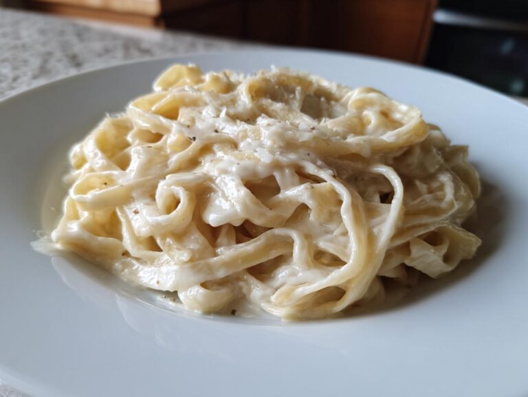 Close-up of fettuccine pasta generously coated in Vegan Creamy Cashew Alfredo Sauce on a white plate.