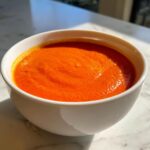 Close-up of a white bowl filled with bright orange Vegan Creamy Tomato Coconut Soup.