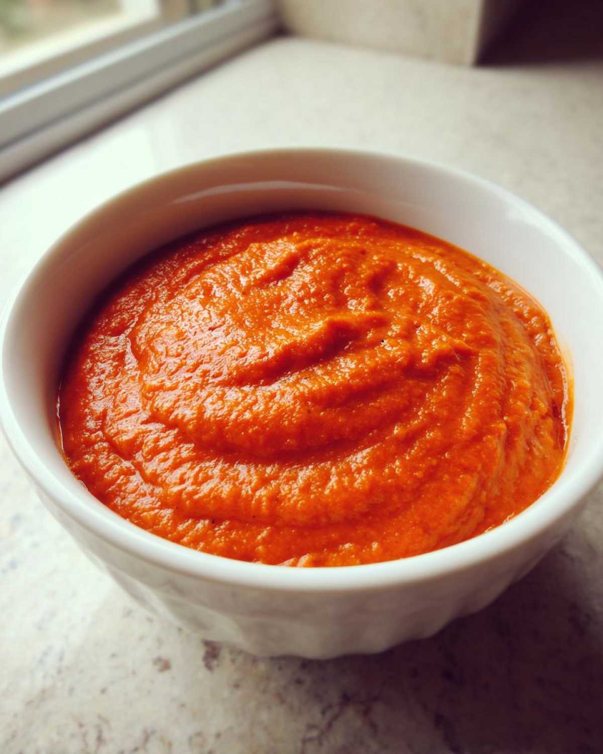 Close-up of thick, vibrant orange Vegan Creamy Tomato Coconut Soup served in a white bowl.
