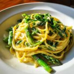 A bright, creamy plate of Vegan Lemon Asparagus Pasta with vibrant green asparagus spears and pea shoots.