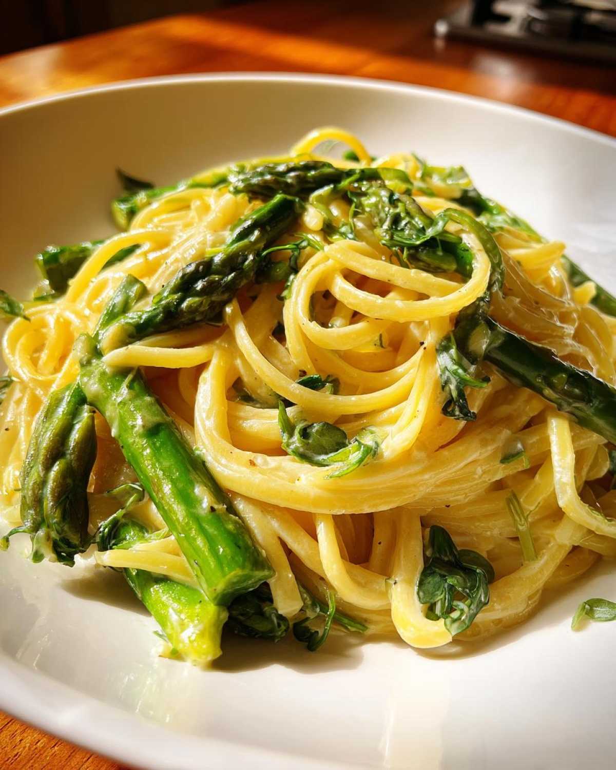 A close-up of creamy Vegan Lemon Asparagus Pasta tossed with bright green asparagus spears and pea shoots.