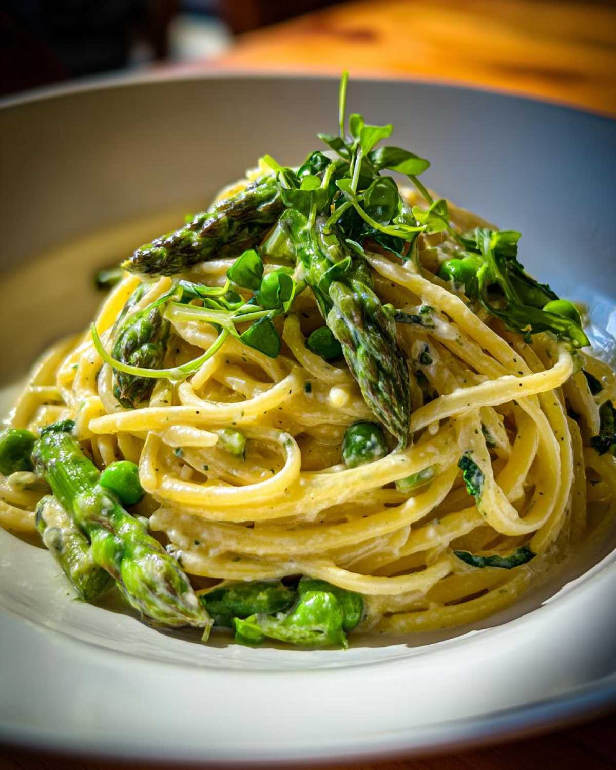 A close-up of creamy Vegan Lemon Asparagus Pasta topped with roasted asparagus spears and fresh pea shoots.