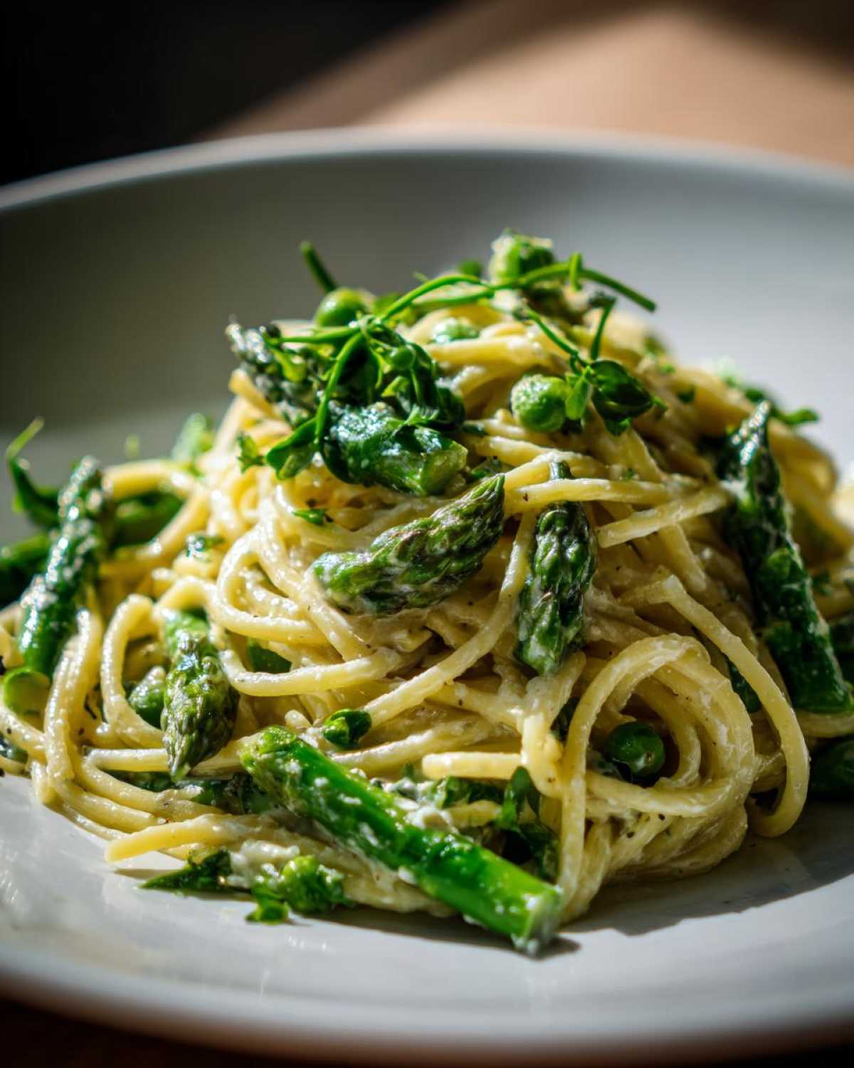 Close-up of creamy Vegan Lemon Asparagus Pasta tossed with bright green asparagus spears and topped with pea shoots.