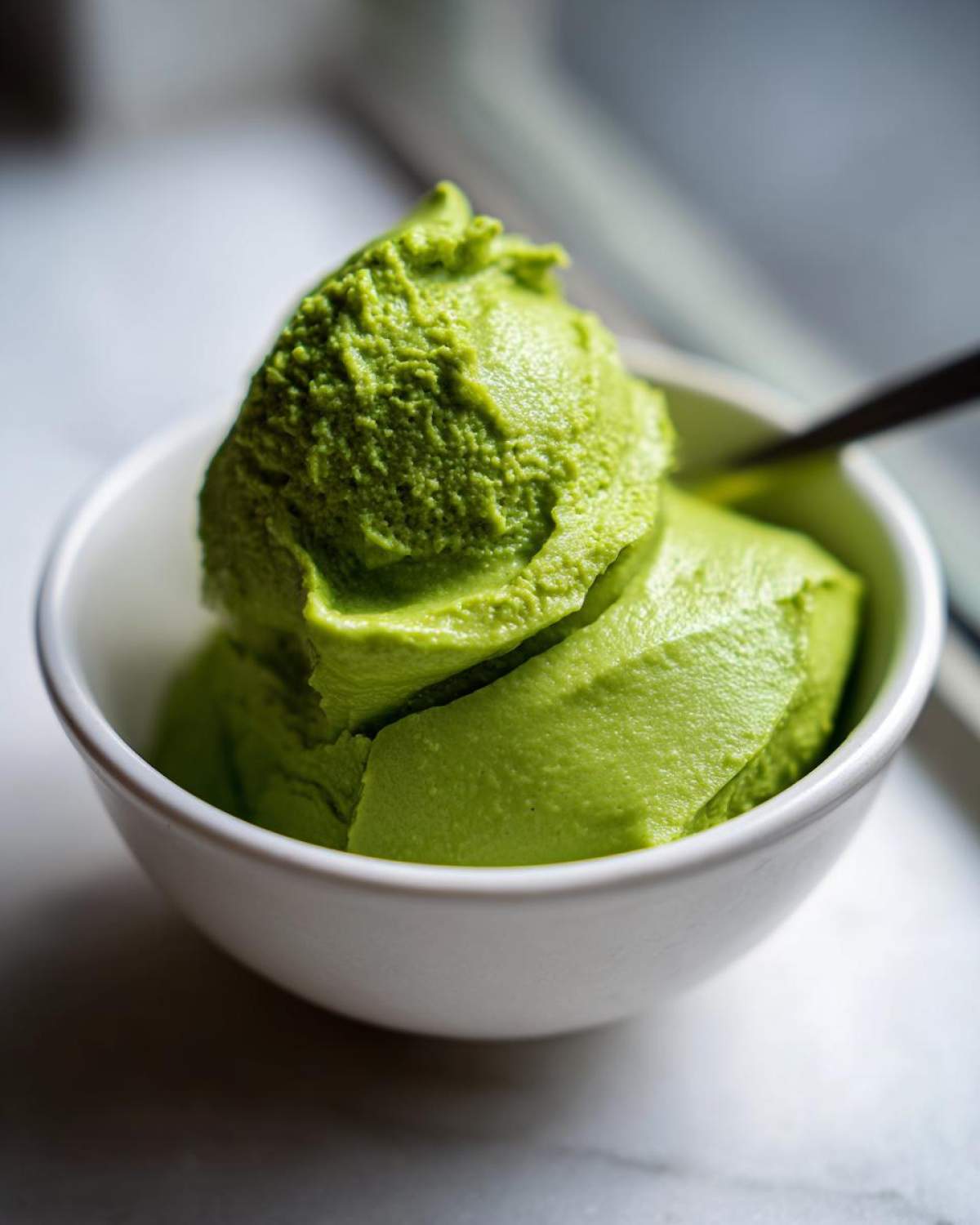 A vibrant green, thick scoop resembling soft-serve or sorbet, likely the Creamy Avocado Cilantro Sauce, in a small white bowl.