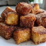 A close-up pile of Air Fryer Crispy Cinnamon French Toast Bites coated heavily in cinnamon sugar.