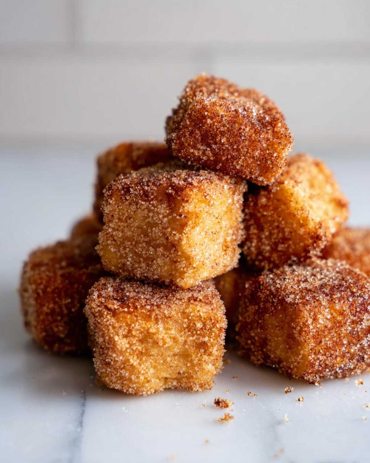 A stack of golden Air Fryer Crispy Cinnamon French Toast Bites coated heavily in cinnamon sugar.