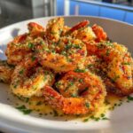 Close-up of golden Air Fryer Crispy Garlic Butter Shrimp coated in breading and parsley, sitting in butter sauce.