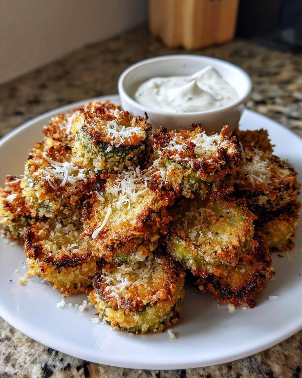 A plate of golden brown Air Fryer Crispy Garlic Dill Pickles topped with grated Parmesan cheese and a dipping sauce.