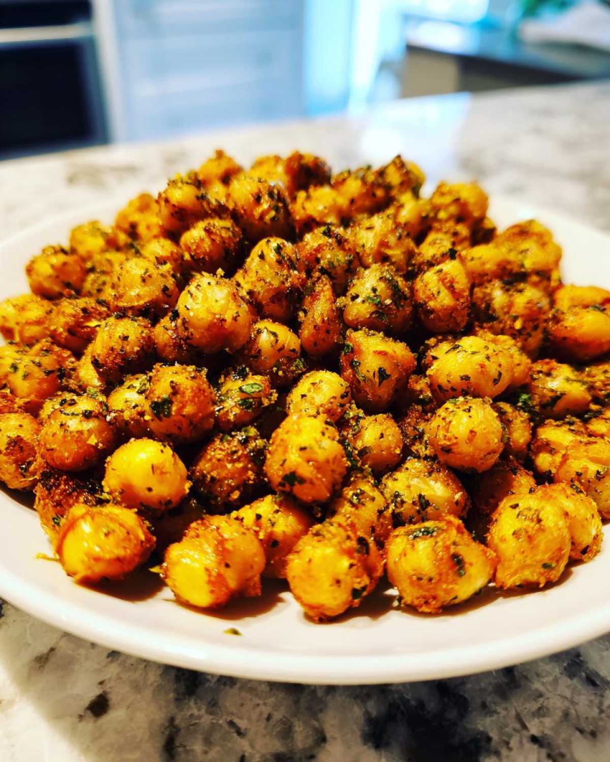 A close-up of golden, crispy Air Fryer Crispy Garlic Herb Chickpeas seasoned with herbs, piled high on a white plate.