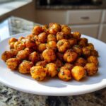 A mound of golden brown Air Fryer Crispy Garlic Herb Chickpeas seasoned with herbs on a white plate.
