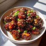 A bowl filled with crispy Air Fryer Crispy Gochujang Brussels Sprouts, coated in a spicy glaze and topped with sesame seeds and green onions.