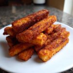 A close-up stack of golden brown, seasoned Air Fryer Crispy Halloumi Fries piled on a white plate.