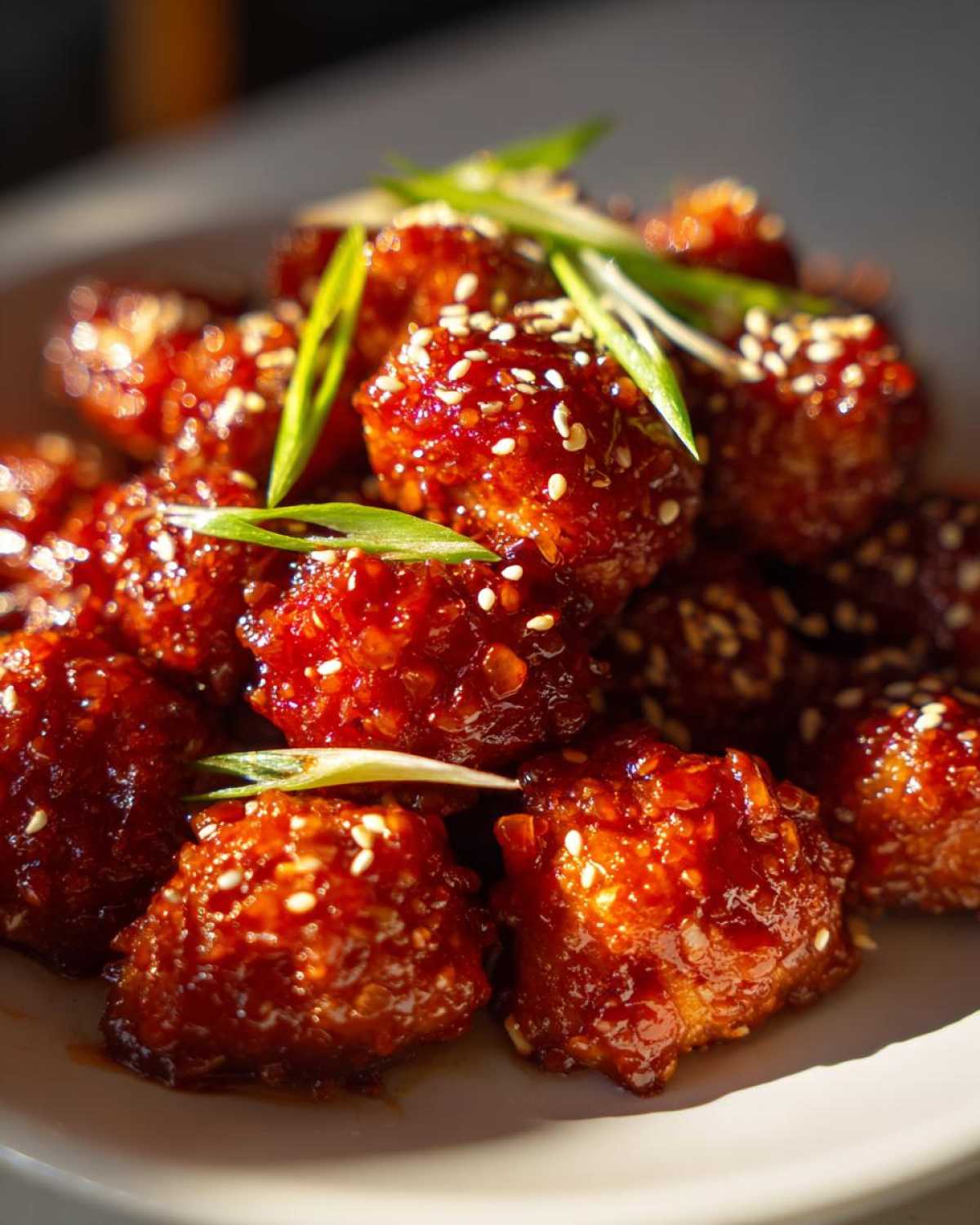 Close-up of glossy, saucy Air Fryer Crispy Korean Chicken Bites garnished with sesame seeds and green onions.