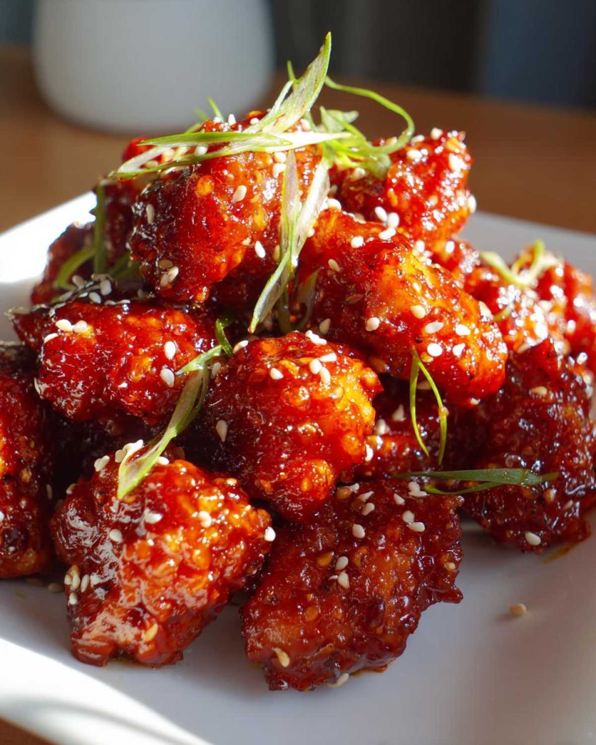 A close-up of glossy, red-glazed Air Fryer Crispy Korean Chicken Bites topped with sesame seeds and green onions.