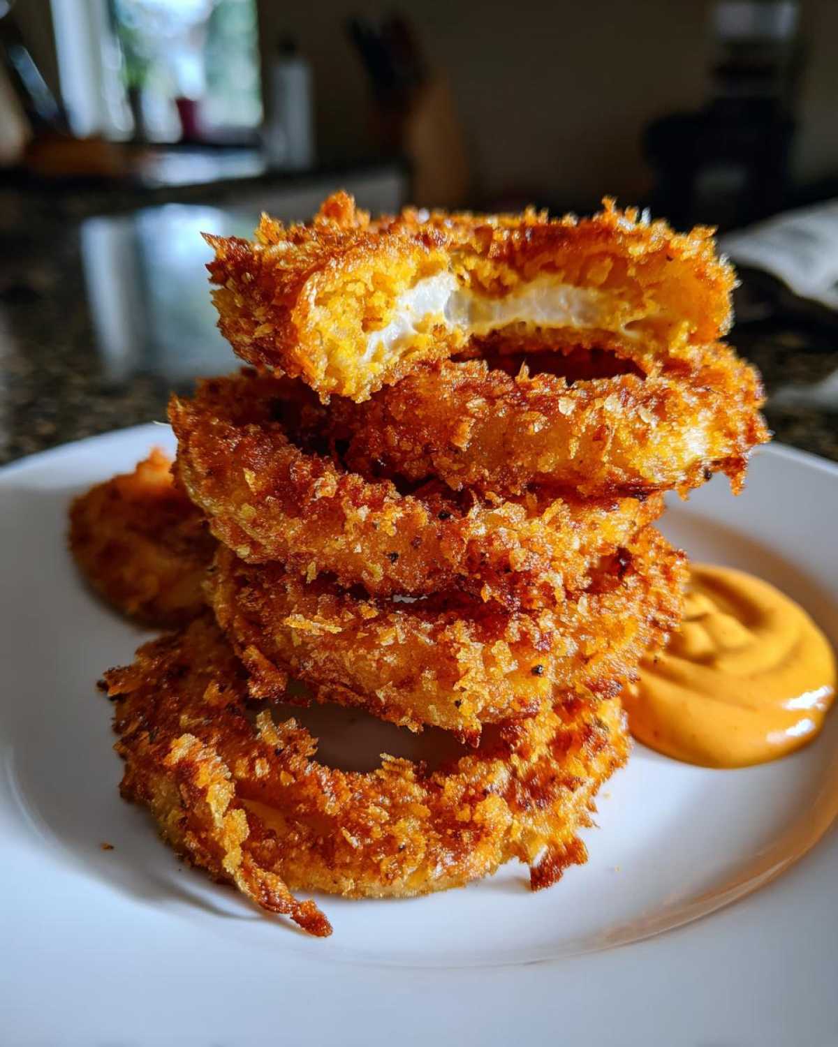 A stack of golden brown Air Fryer Crispy Onion Petals served with a dollop of orange spicy mayo on a white plate.