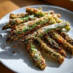 A pile of Air Fryer Crispy Parmesan Asparagus Fries, perfectly browned and topped with grated cheese, served on a white plate.