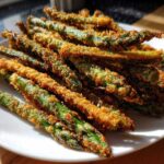 A pile of golden brown Air Fryer Crispy Parmesan Asparagus Fries served on a white plate.