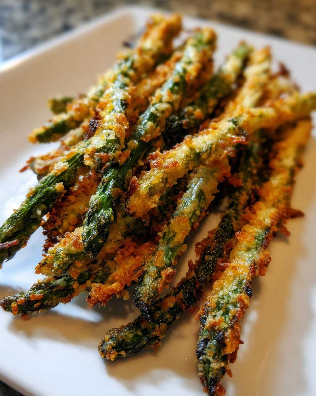 Close-up of perfectly cooked Air Fryer Crispy Parmesan Asparagus Fries piled on a white plate.