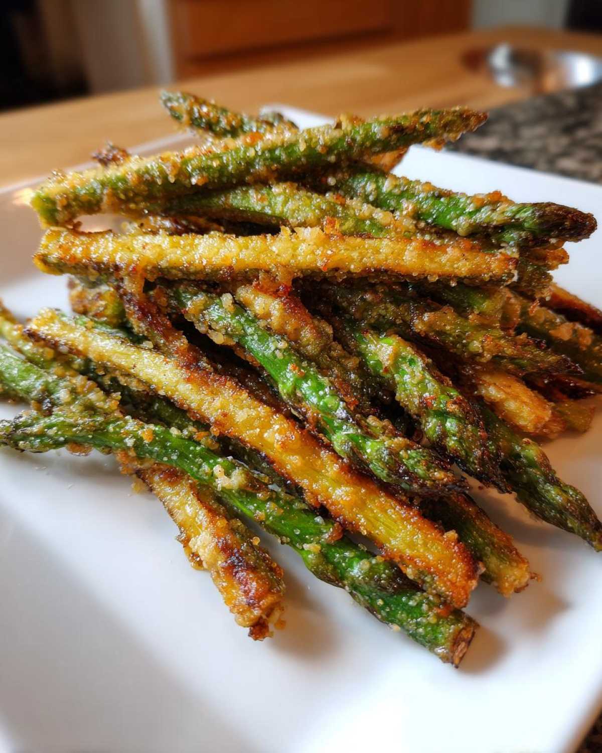 A close-up pile of golden brown and green Air Fryer Crispy Parmesan Asparagus Fries on a white serving dish.
