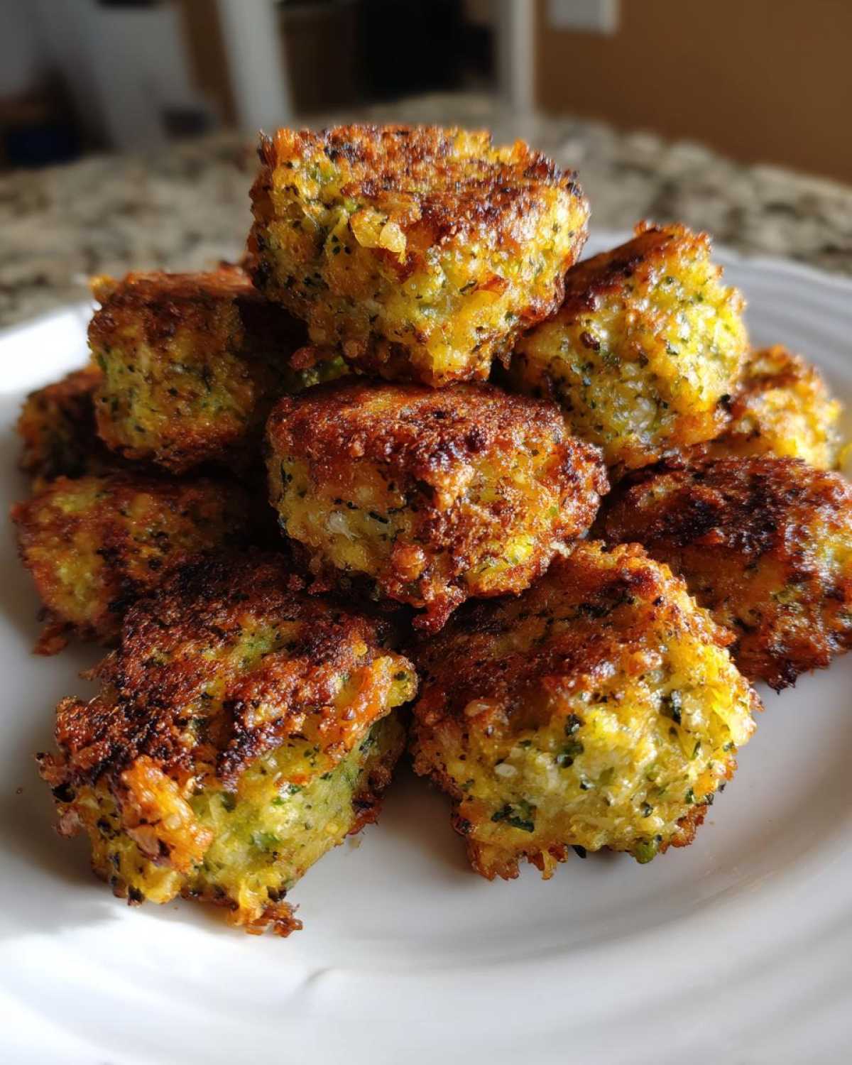 A pile of golden brown Air Fryer Crispy Parmesan Broccoli Tots stacked on a white plate.